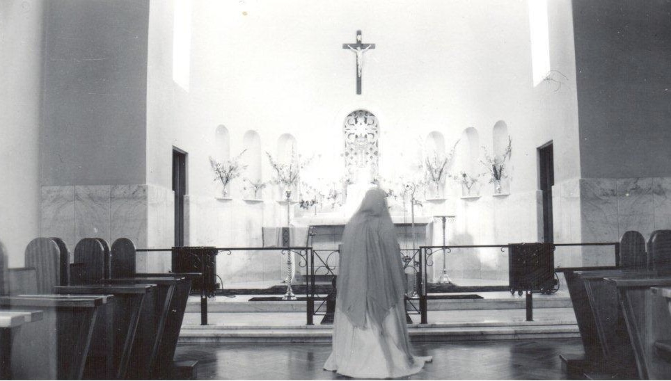 Image 1 of 4 - A photograph of a Sister from the Little Company of Mary kneeling in prayer at the altar of the Chapel of the Maternal Heart of Mary which was opened in 1952. The sister is wearing white robes and the distinctive blue veil that the Little Company of Mary is known for.