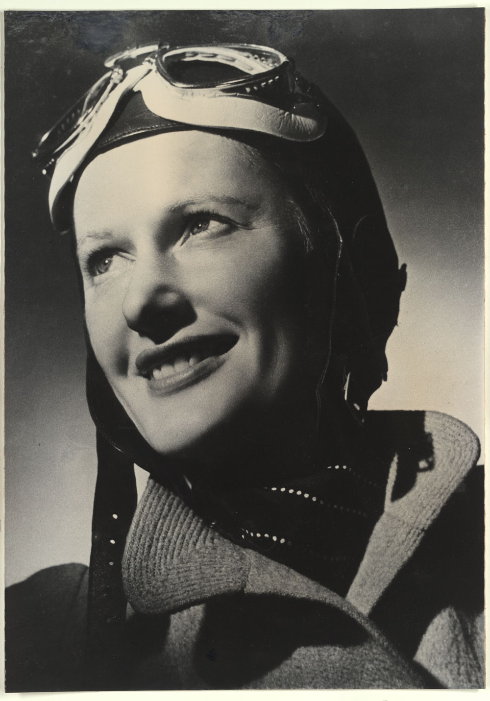 Formal posed black-and-white photo of Nancy Bird Walton wearing an aviation cap, with goggles pushed up over her forehead. She is dressed in a thick jacket.