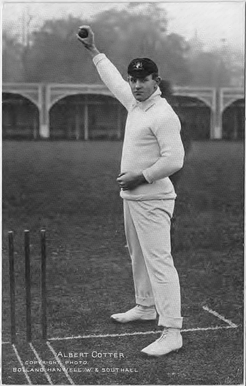 Image 5 of 6 - Tibby Cotter in all white cricket uniform, holding up a cricket ball next to cricket stumps.