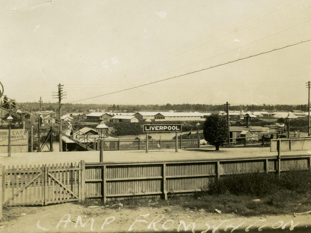 Image 3 of 6 - Black and white image of Liverpool army camp. In the middle of the image there is a sign that says ‘LIVERPOOL’. There is a fence in the foreground and a telegraph pole line going across the image.
