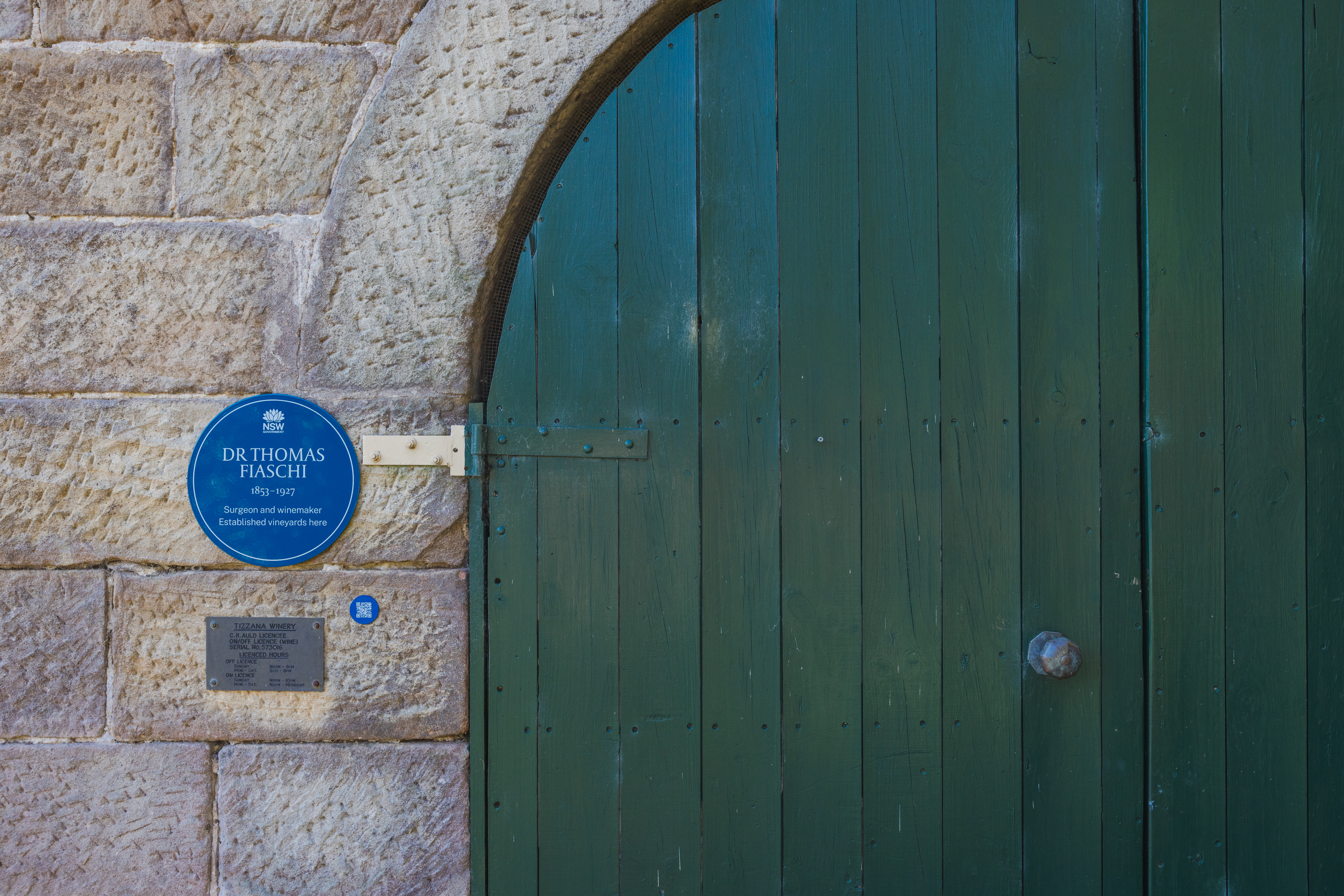 Image 6 of 6 - A photo of a blue plaque on a sandstone wall to the left of a green barn door