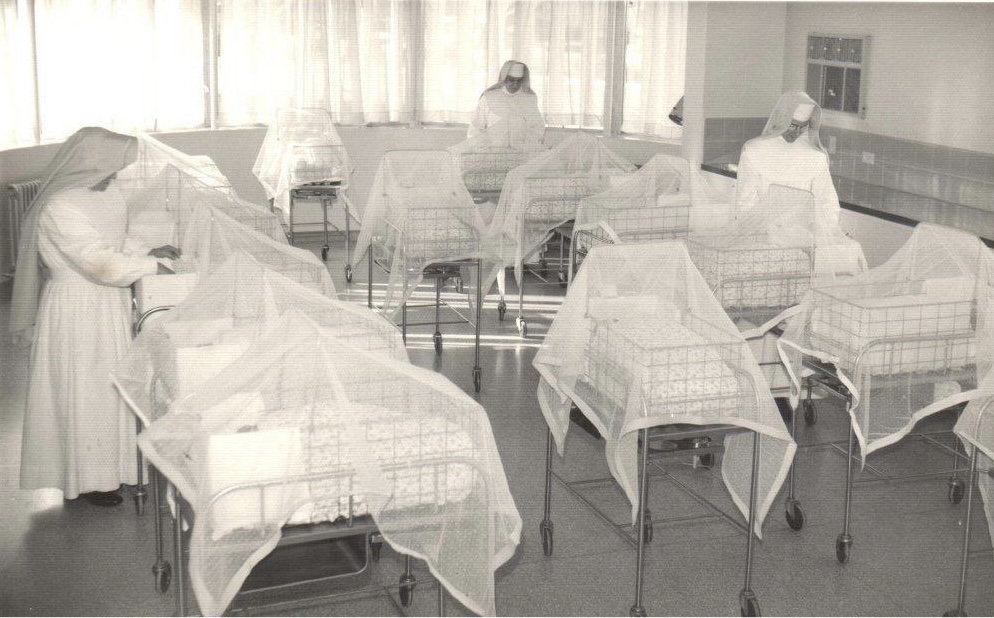 A photograph of three Sisters of the Little Company of Mary attending to newborn babies in cribs in the hospital’s maternity ward which operated between 1959 and 1988 