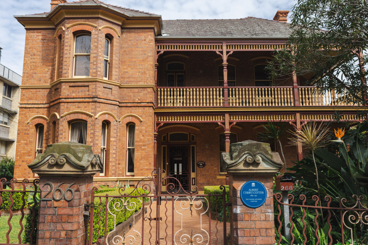 Image 6 of 6 - An image of a blue plaque installed on a brick post outside a large old house