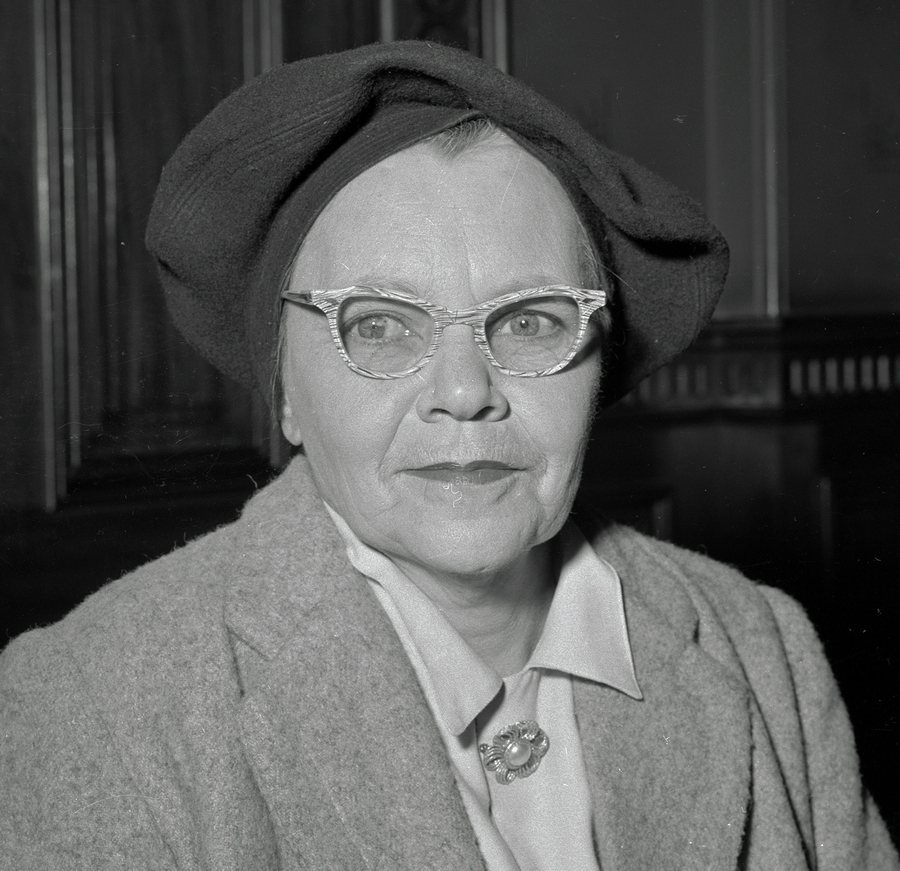 A black and white photograph of a woman wearing glasses and a hat