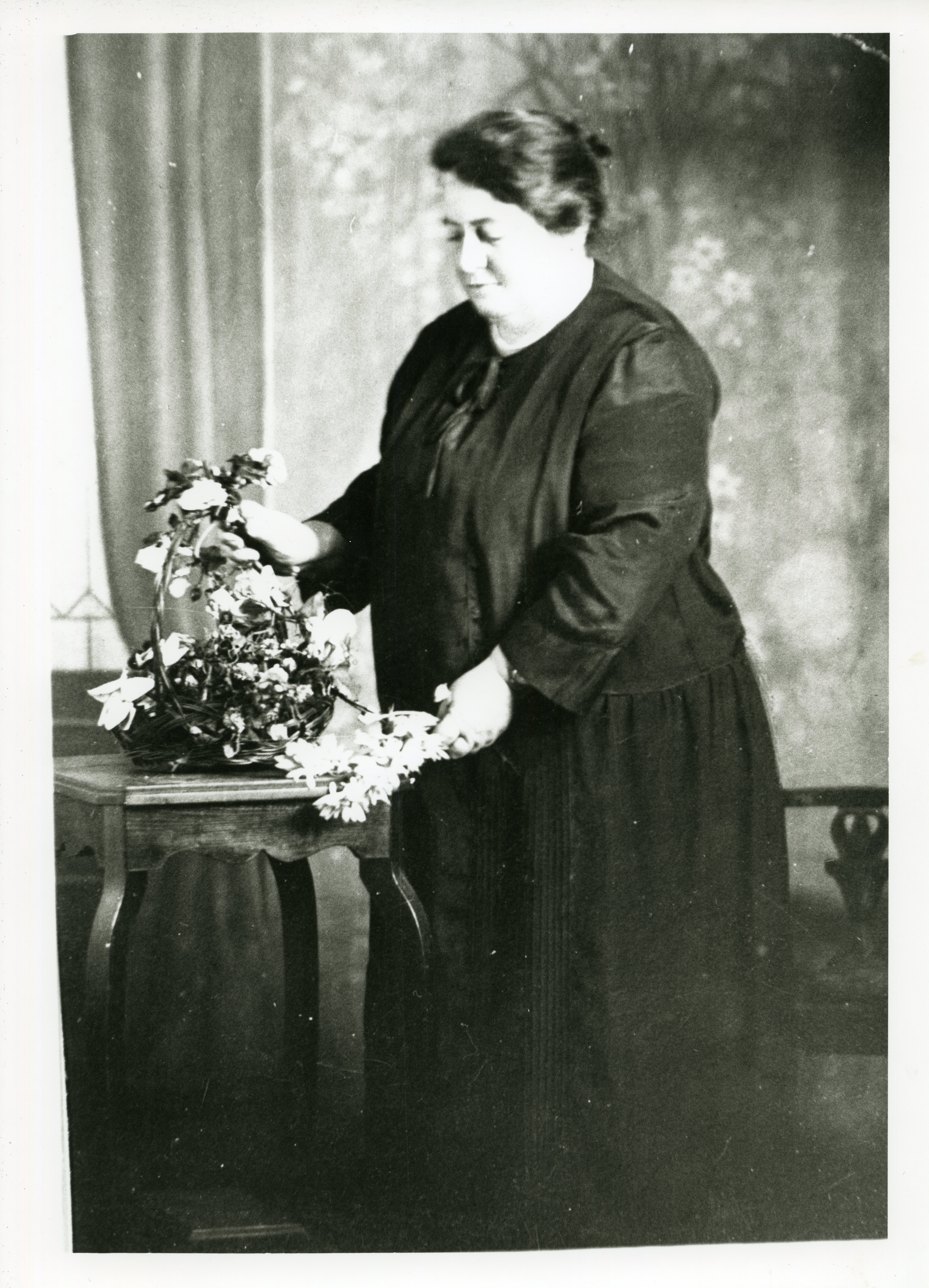 Image 2 of 4 - Black and white photo of a woman arranging flowers on a small wooden side table.