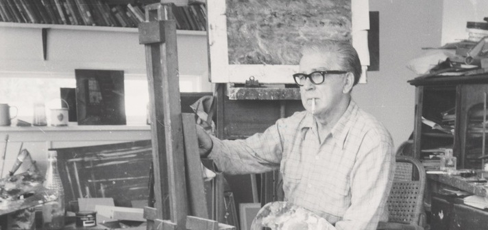 Black and white photograph of a man sitting down and painting on an easel with a cigarette in his mouth