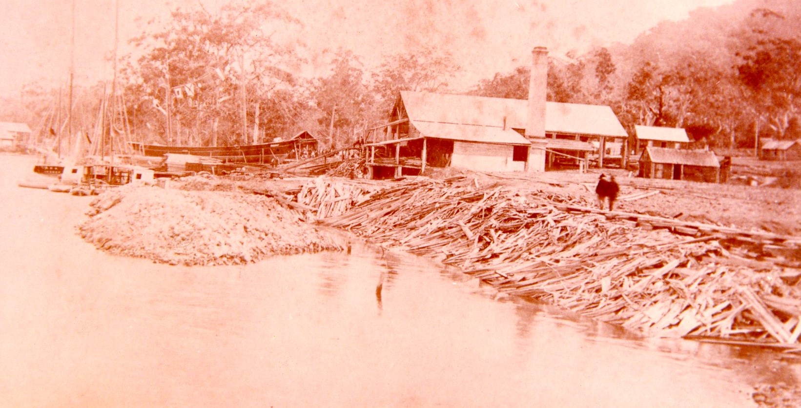 A sepia image of the timber mill owned and operated by Joseph Laurie in Laurieton taken in 1886. Two men can be seen walking along the bank and the ship “Our Elsie” sits in the slipway behind the building.