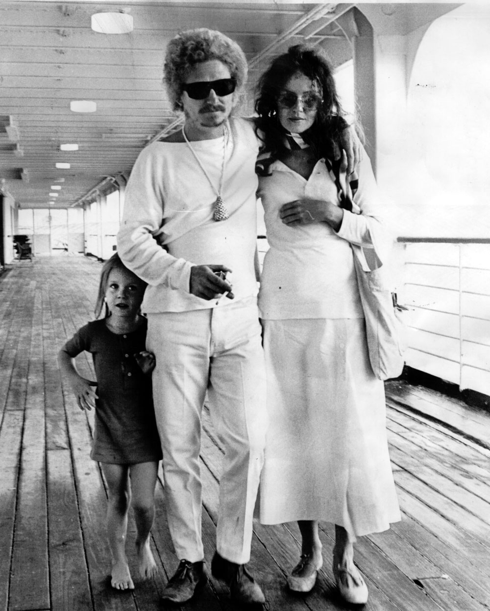 A photograph of the Whiteley Family returning to Sydney. Brett has his arm around Wendy and their daughter, Arkie, playfully hides behind him.