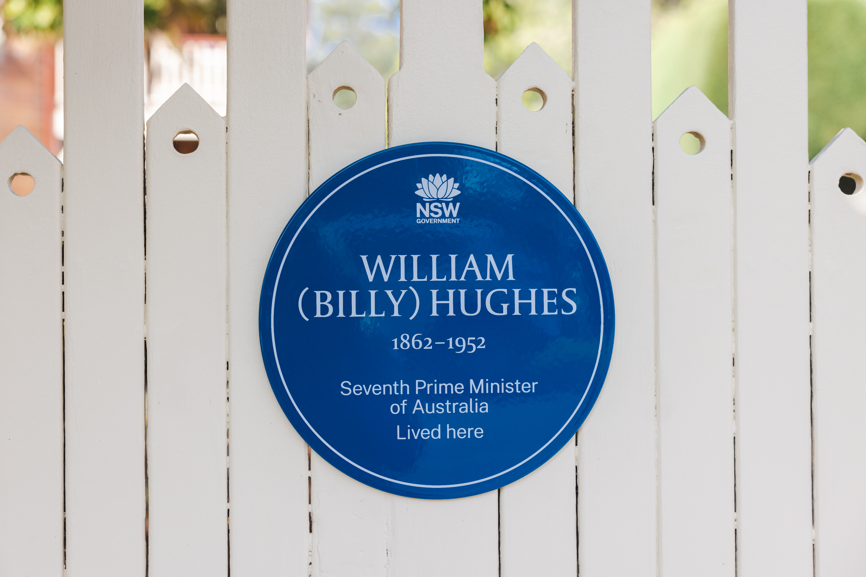 Image 6 of 6 - A blue plaque for Billy Hughes on a white picket fence gate