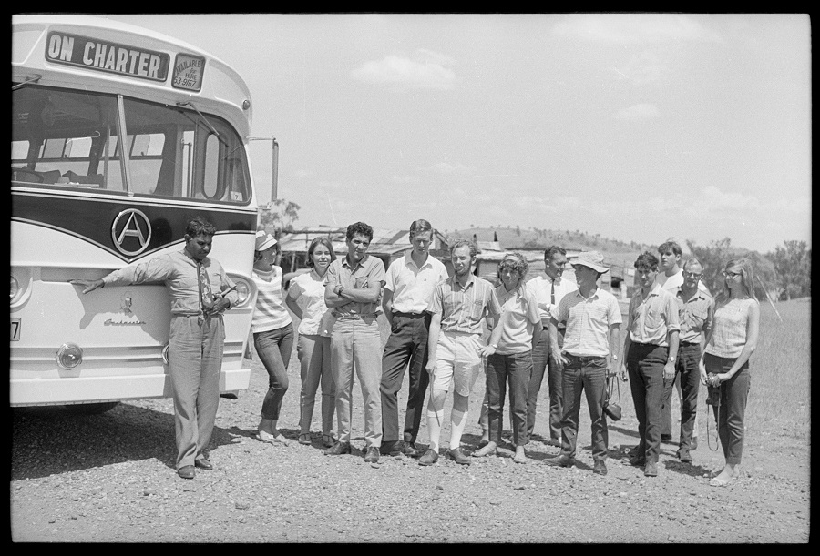 Black and white photograph of people standing alongside a bus