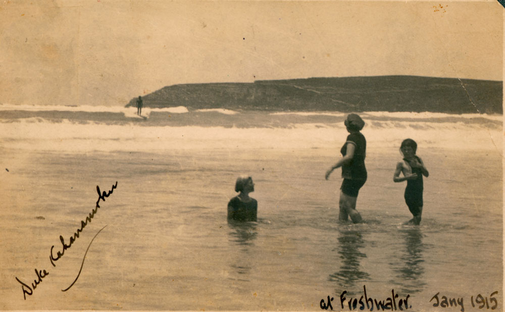 Image 4 of 6 - This 1915 photograph by Isabel Letham shows Duke Kahanamoku surfing at Freshwater Beach. Three swimmers in the foreground look out to Duke on the waves. The photographer has written on the front of the photo “Duke Kahanamoku, 1915”