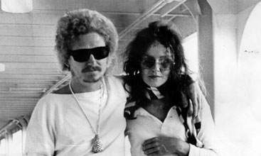 Man in sunglasses with light-coloured curly hair next to a woman in sunglasses with long dark hair