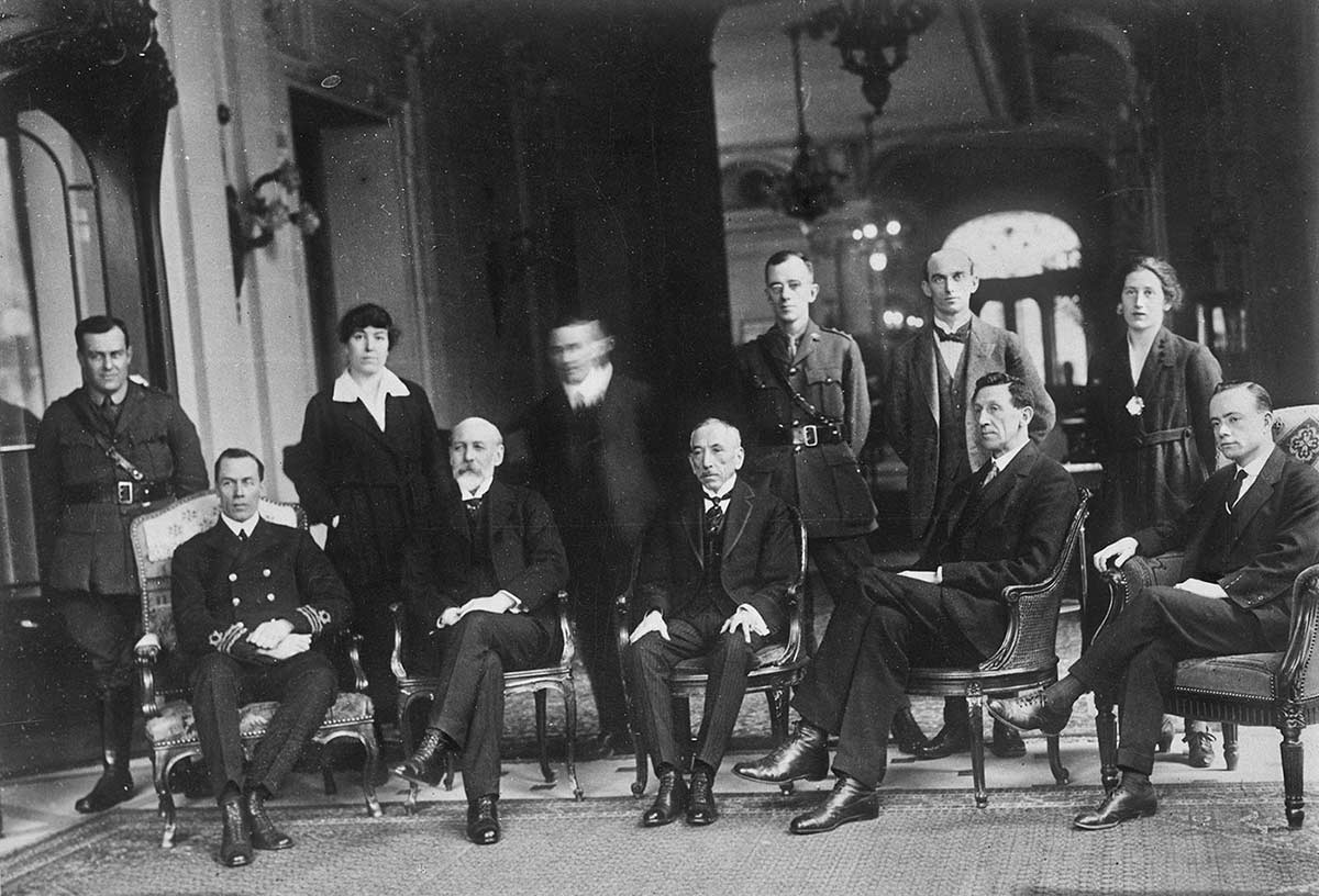 Image 3 of 6 - Black and white image of four men and two women standing behind 5 men sitting on chairs.