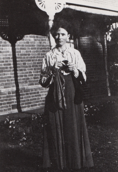 Image 1 of 6 - Black and white portrait of a woman outside wearing a shirt and a long skirt.