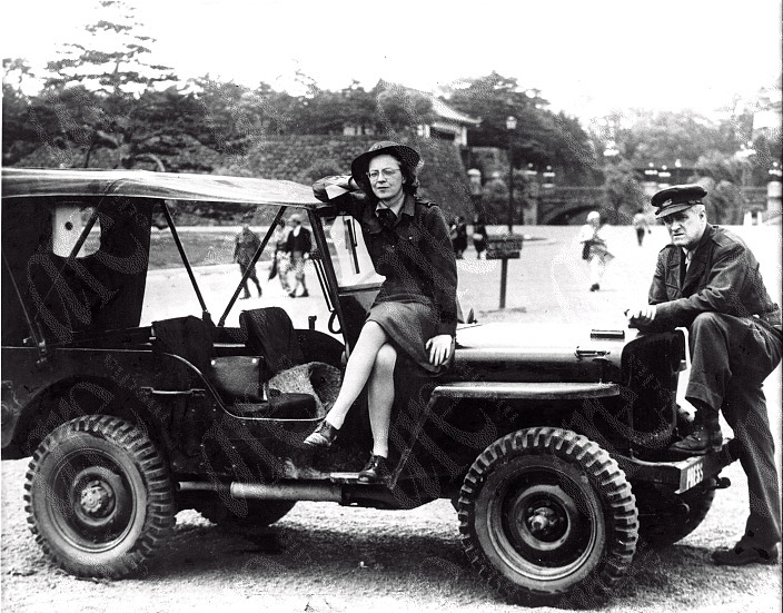 A woman sitting on a jeep and a man leaning his leg against it