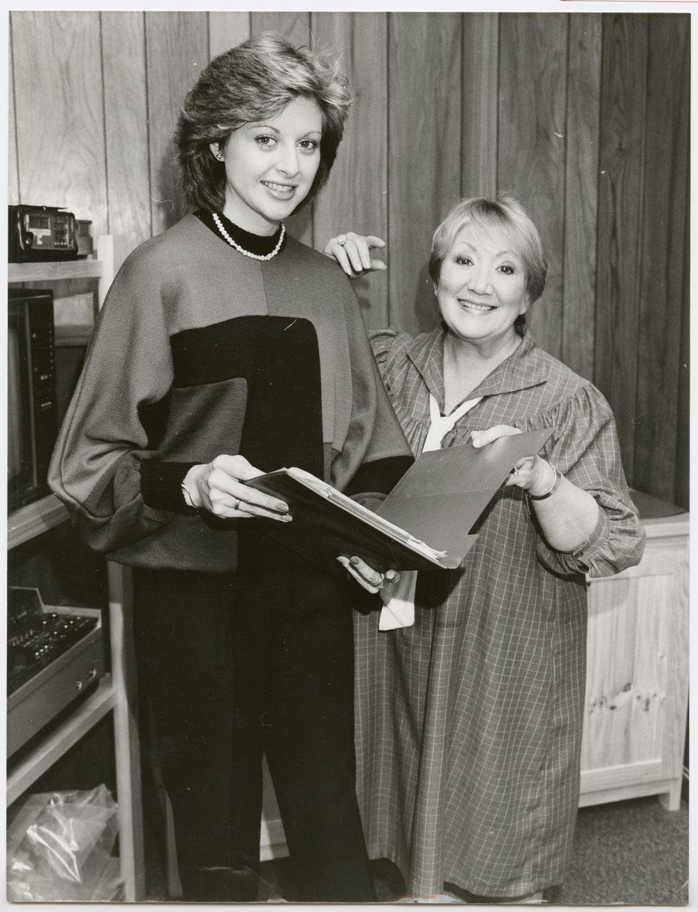 Image 1 of 5 - Photograph of June Bronhill taken when she was a guest on the television program “Adelaide Today” hosted by Amanda Halvorse. June and Amanda stand next to each other holding open between them a folder with some papers.