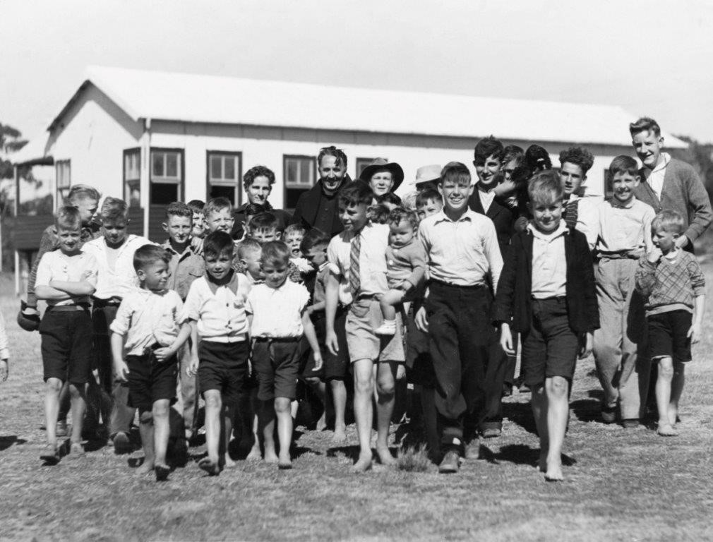 Image 1 of 5 - A young Father Dunlea with a large group of boys of all ages standing in front of a building at Boys Town in Engadine, now known as the Dunlea Centre.
