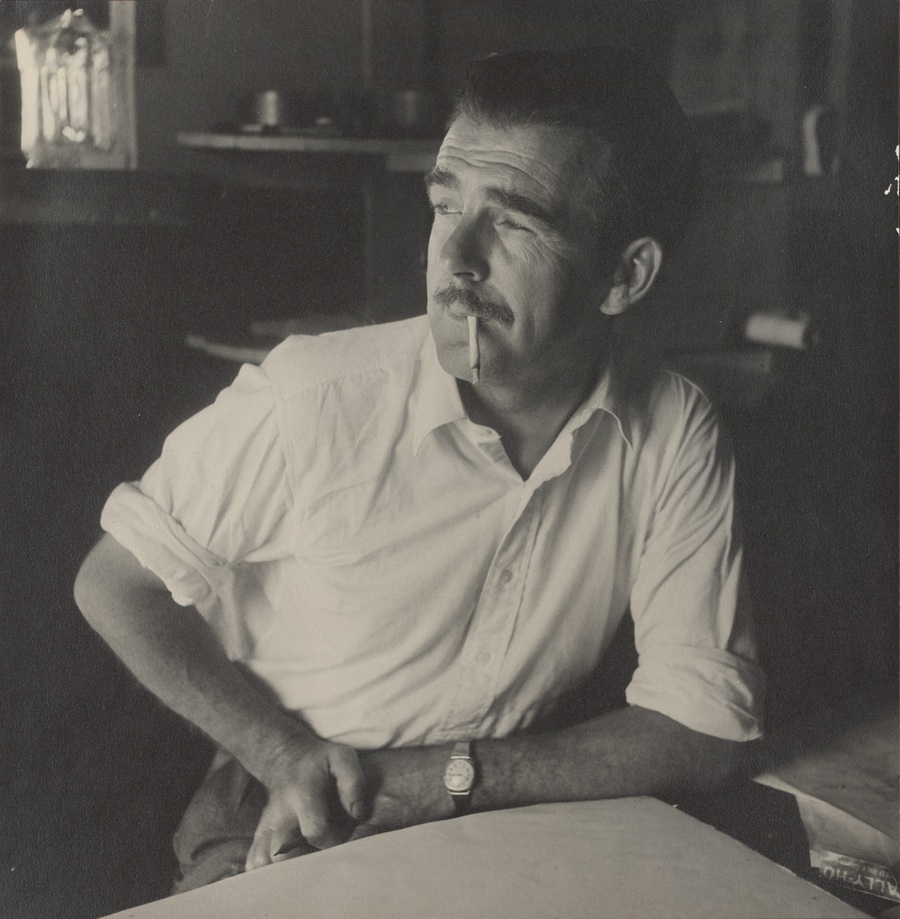 Image 1 of 2 - A black and white image of a man with his arm resting on a desk and a cigarette in his mouth